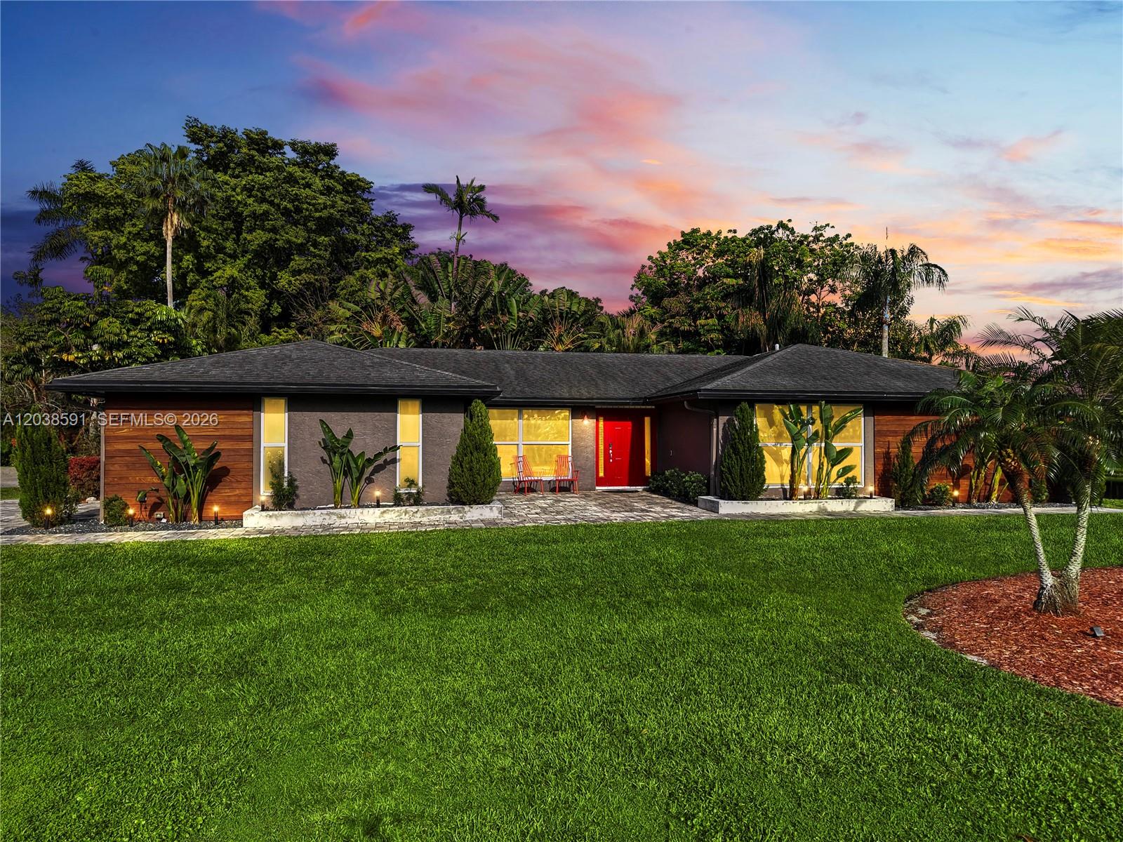 A single-story house with a red front door, dark siding, and a large front lawn — DAVIE, FL