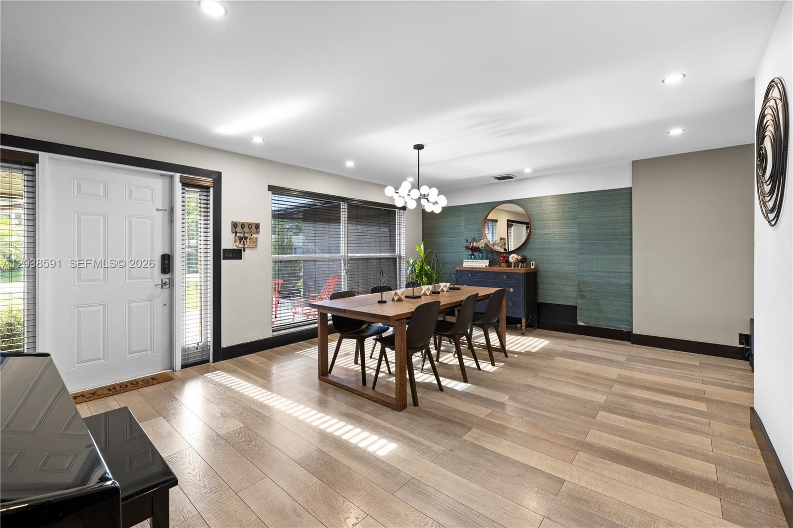 A dining room features a wooden table, modern chandelier, and a textured green accent wall — DAVIE, FL