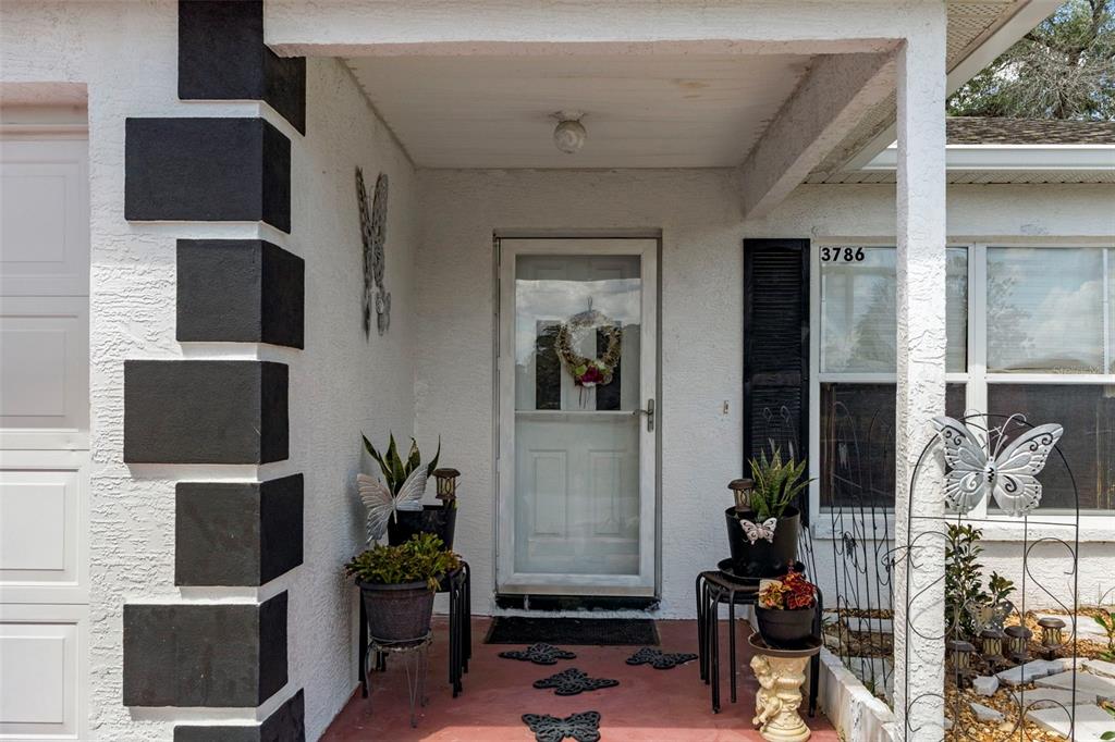 A covered front porch features a white door, potted plants, and butterfly-themed decor — 3786 S GREY DOVE TERRACE, HOMOSASSA, FL