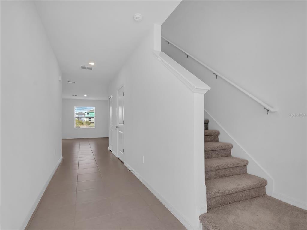 A hallway with tile flooring leads to a window, with carpeted stairs on the right — 5757 RED KITE DRIVE, WIMAUMA, FL