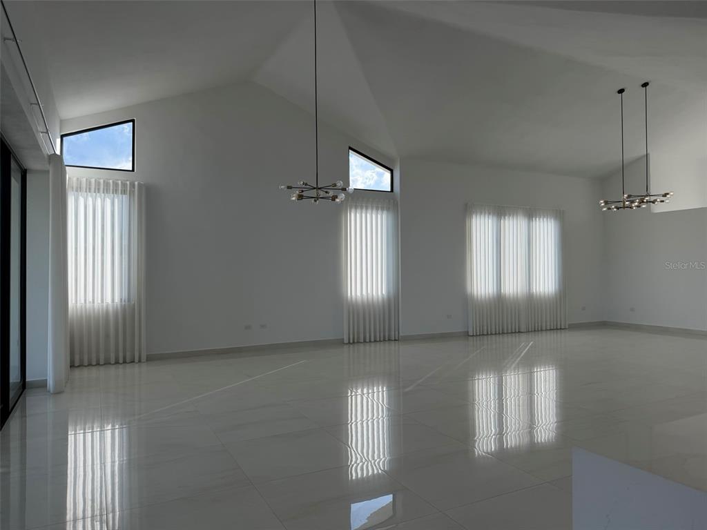 A spacious, minimalist living room features white walls, vaulted ceilings, tiled floors, and modern chandeliers — 927 SABANERA ISLA NORTE, DORADO, PR