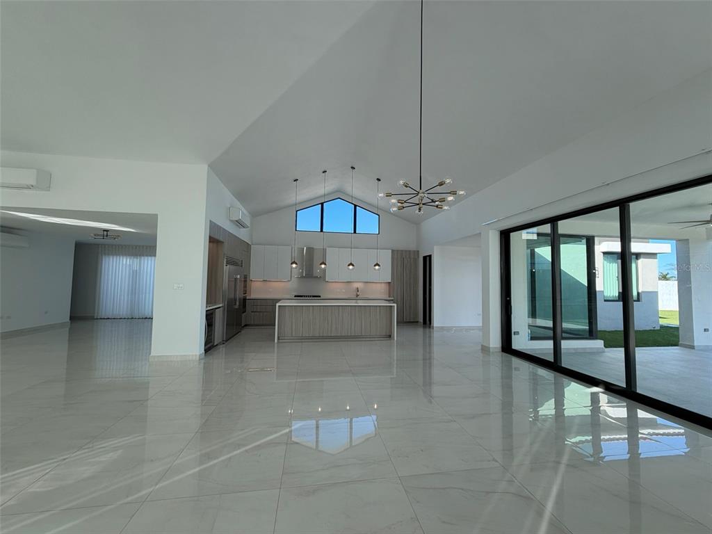 A modern open-concept kitchen and living area features vaulted ceilings, tile floors, and glass walls — 927 SABANERA ISLA NORTE, DORADO, PR