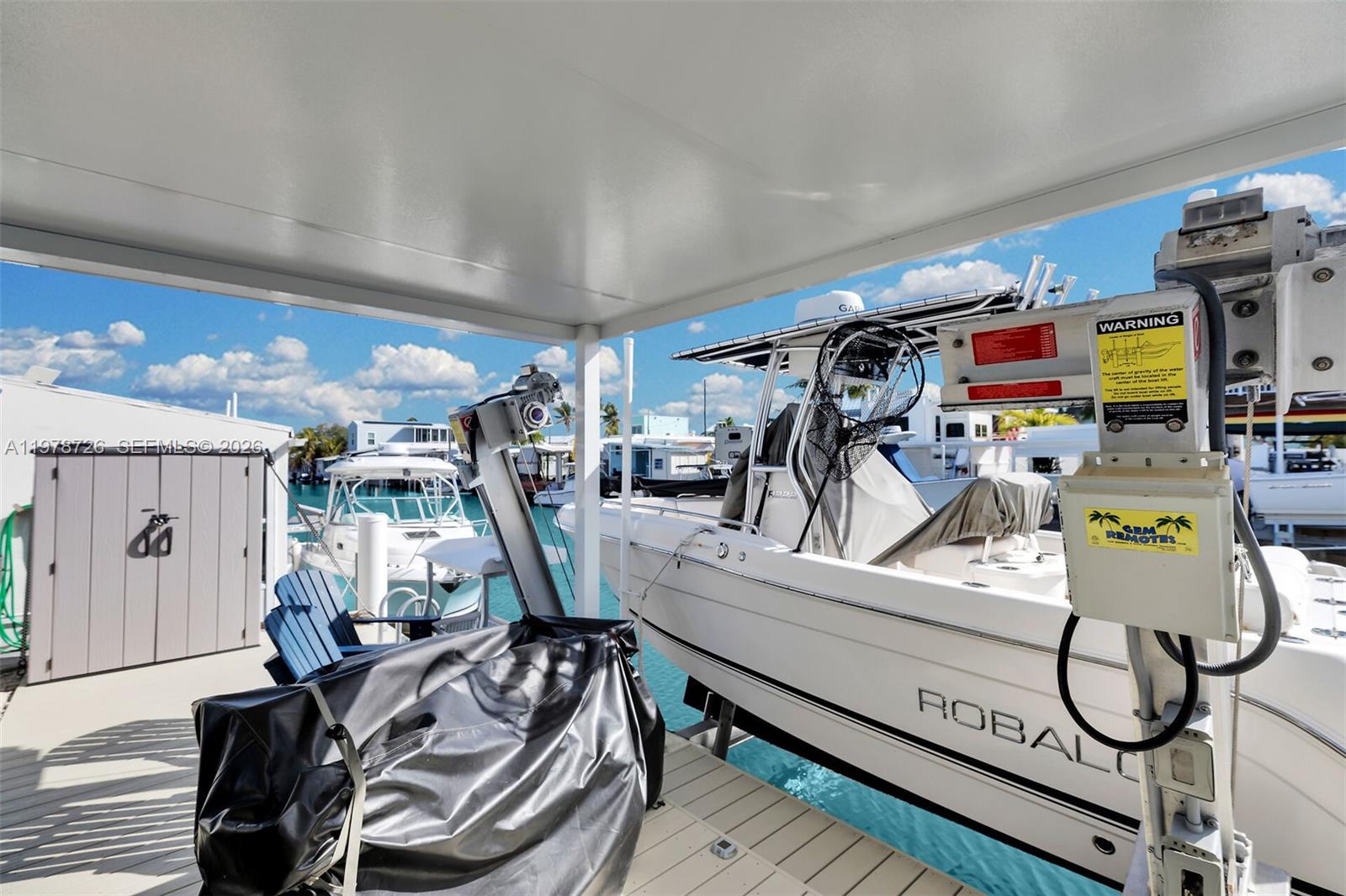 A white boat is docked under a covered pier with a storage shed nearby — 6099 Overseas Hwy 55W, Marathon FL 33050, MARATHON, FL
