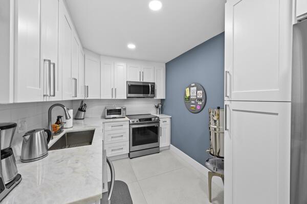 A modern kitchen features white cabinets, marble countertops, stainless steel appliances, and a blue accent wall — 10137 S 40th Way # 233, Boynton Beach FL 33436, BOYNTON BEACH, FL