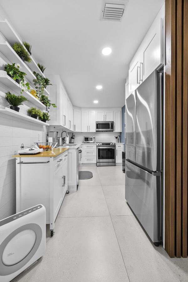 A modern galley kitchen features white cabinetry, stainless steel appliances, and open shelving with plants — 10137 S 40th Way # 233, Boynton Beach FL 33436, BOYNTON BEACH, FL