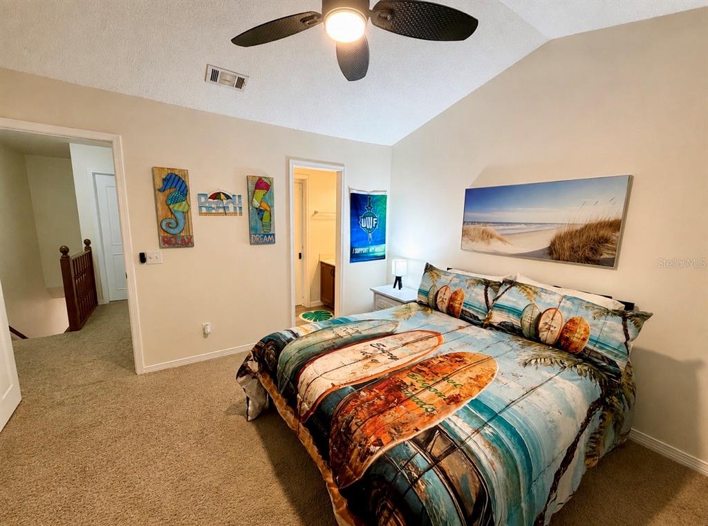 A bedroom features a surfboard-themed comforter, a beach landscape wall art, and a ceiling fan — 10105 VIXEN PLACE, PENSACOLA, FL