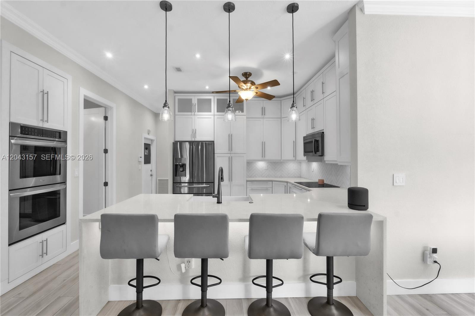 A modern kitchen features white cabinetry, a central island with bar seating, and pendant lighting — 720 S Old Nob Hill Rd, Plantation FL 33324, PLANTATION, FL