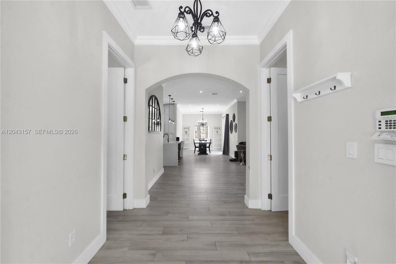 A hallway with light wood-look flooring leads through an arched doorway into an open-concept living area — 720 S Old Nob Hill Rd, Plantation FL 33324, PLANTATION, FL