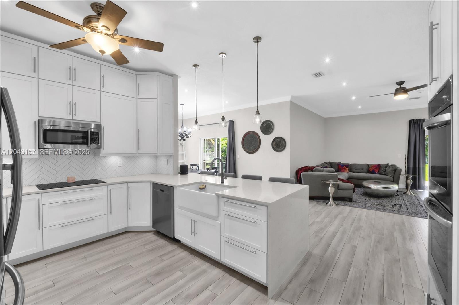 A modern kitchen with white cabinets and a farmhouse sink opens to a living area — 720 S Old Nob Hill Rd, Plantation FL 33324, PLANTATION, FL