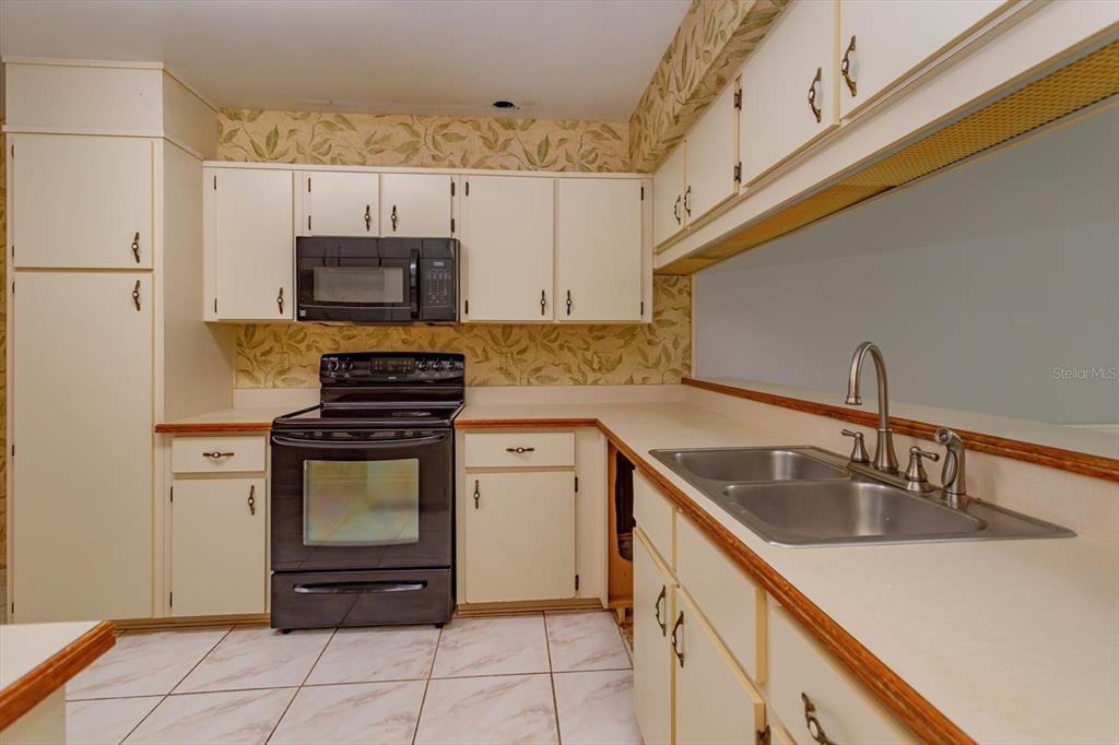 A kitchen features off-white cabinets, black appliances, patterned wallpaper, and a double stainless steel sink — 8266 AMBROSE COVE WAY, ORLANDO, FL