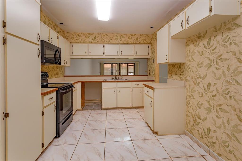 A kitchen with white cabinets, patterned wallpaper, tile flooring, and a black oven — 8266 AMBROSE COVE WAY, ORLANDO, FL