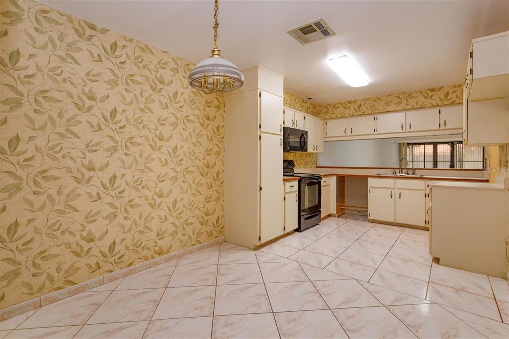 A kitchen and dining area with leaf-patterned wallpaper, white cabinets, and diagonal floor tiles — 8266 AMBROSE COVE WAY, ORLANDO, FL