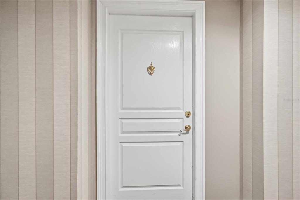 A white door with a gold knocker and handle is set between two textured walls — 750 N TAMIAMI TRAIL UNIT 312, SARASOTA, FL