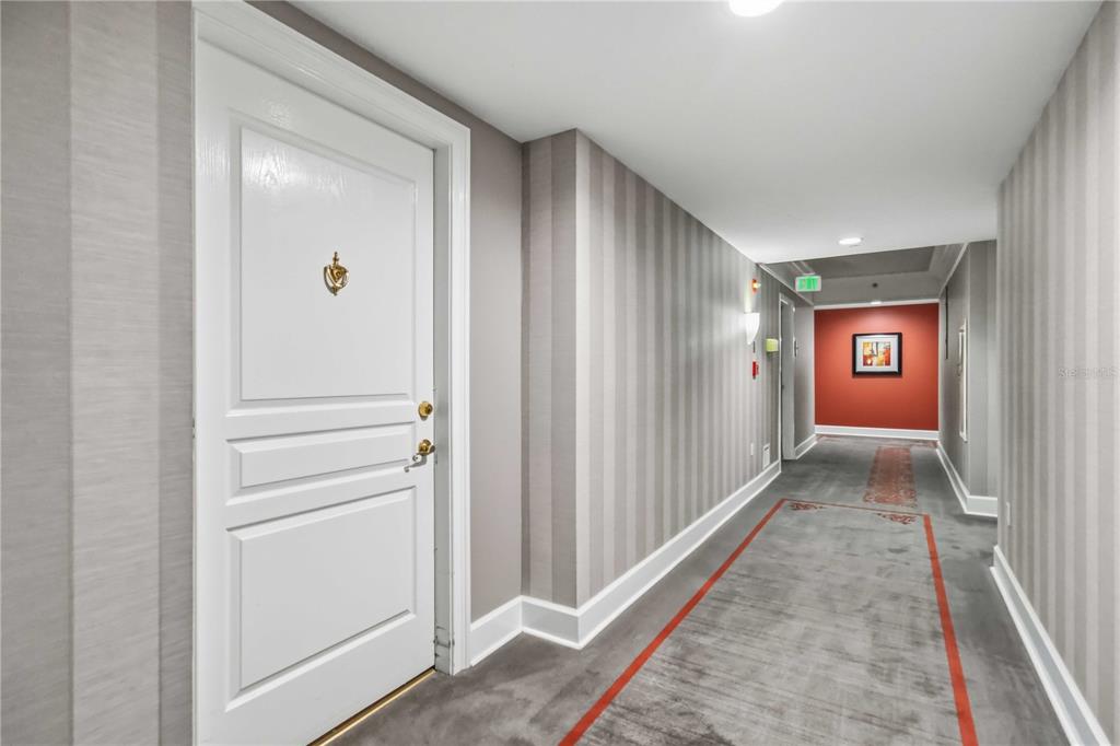 A hallway with striped wallpaper, gray carpeting, and a white door with a gold knocker — 750 N TAMIAMI TRAIL UNIT 312, SARASOTA, FL