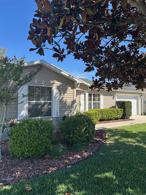 A tan, single-story house with white shutters, a garage, and landscaped bushes in the front — 17353 SE 76TH FLINTLOCK TERRACE, THE VILLAGES, FL