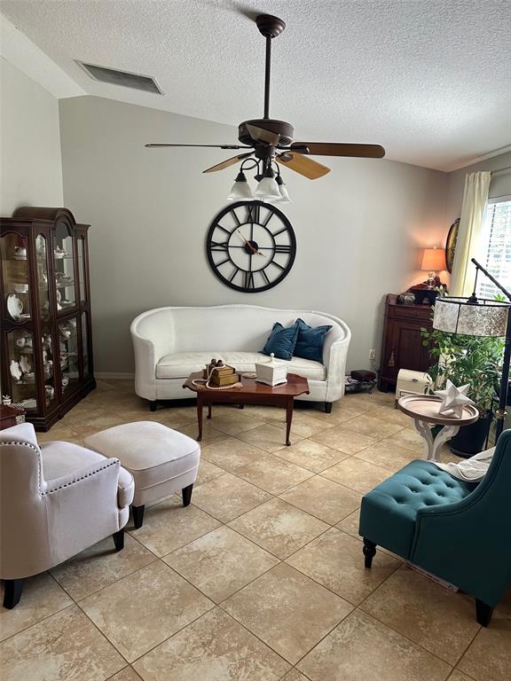 A living room features a white sofa, a teal armchair, a ceiling fan, and tile flooring — 17353 SE 76TH FLINTLOCK TERRACE, THE VILLAGES, FL