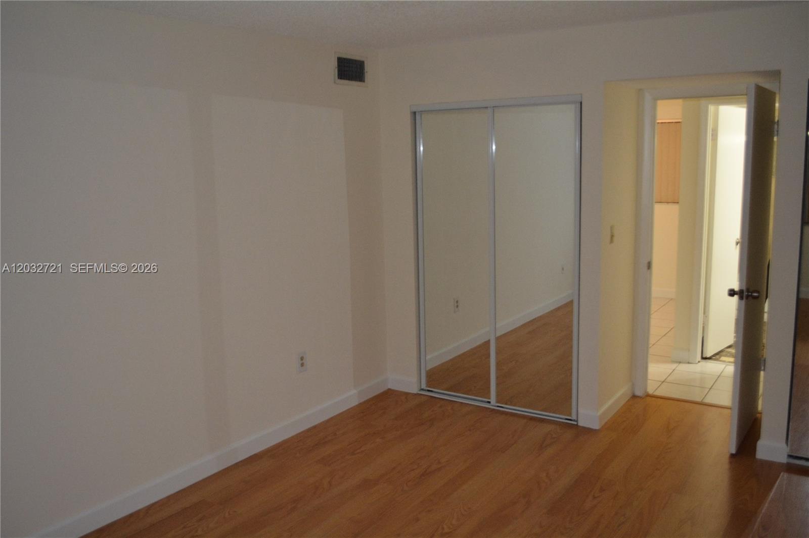 This bedroom features light-colored walls, wood-look flooring, a mirrored closet, and an open doorway — 13100 SW 92nd Ave, Miami FL 33176, MIAMI, FL