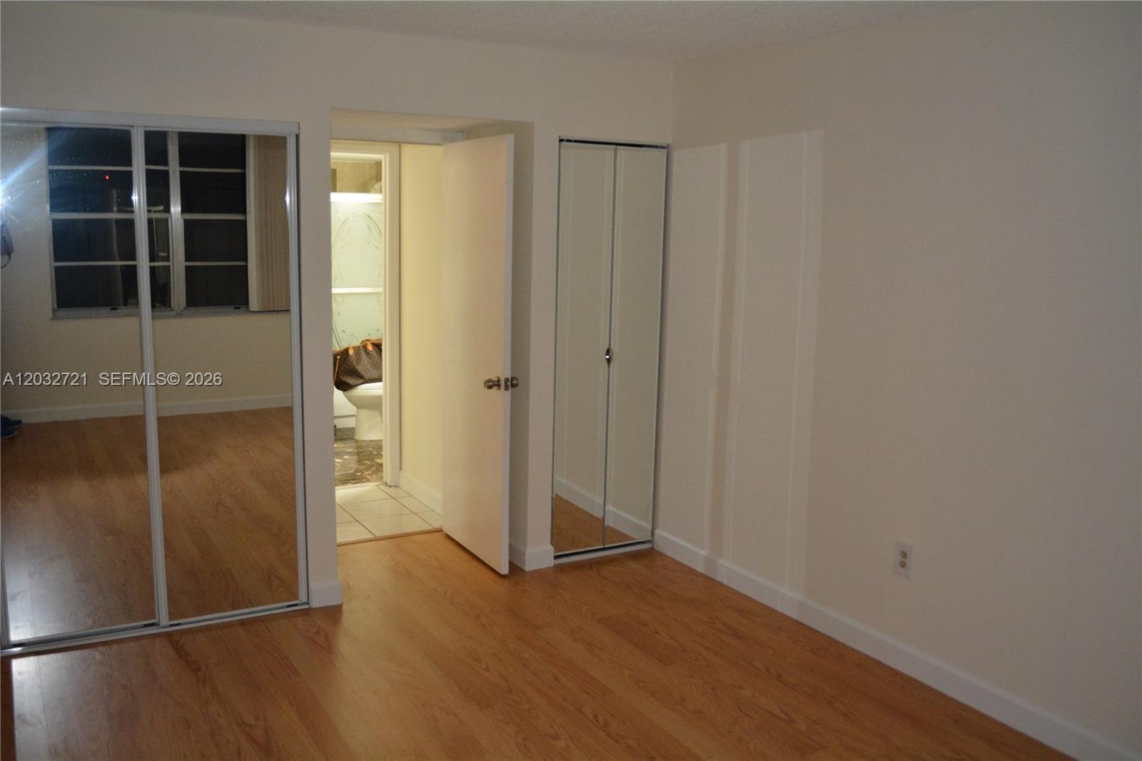 A bedroom features wood-look flooring, mirrored closet doors, and an open doorway to a bathroom — 13100 SW 92nd Ave, Miami FL 33176, MIAMI, FL
