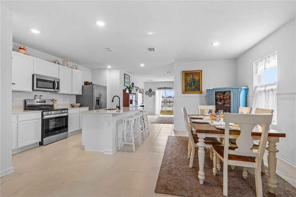 An open-concept kitchen and dining area with white cabinets, stainless appliances, and tile flooring — 1192 BELLE ISLE LANE, DAYTONA BEACH, FL