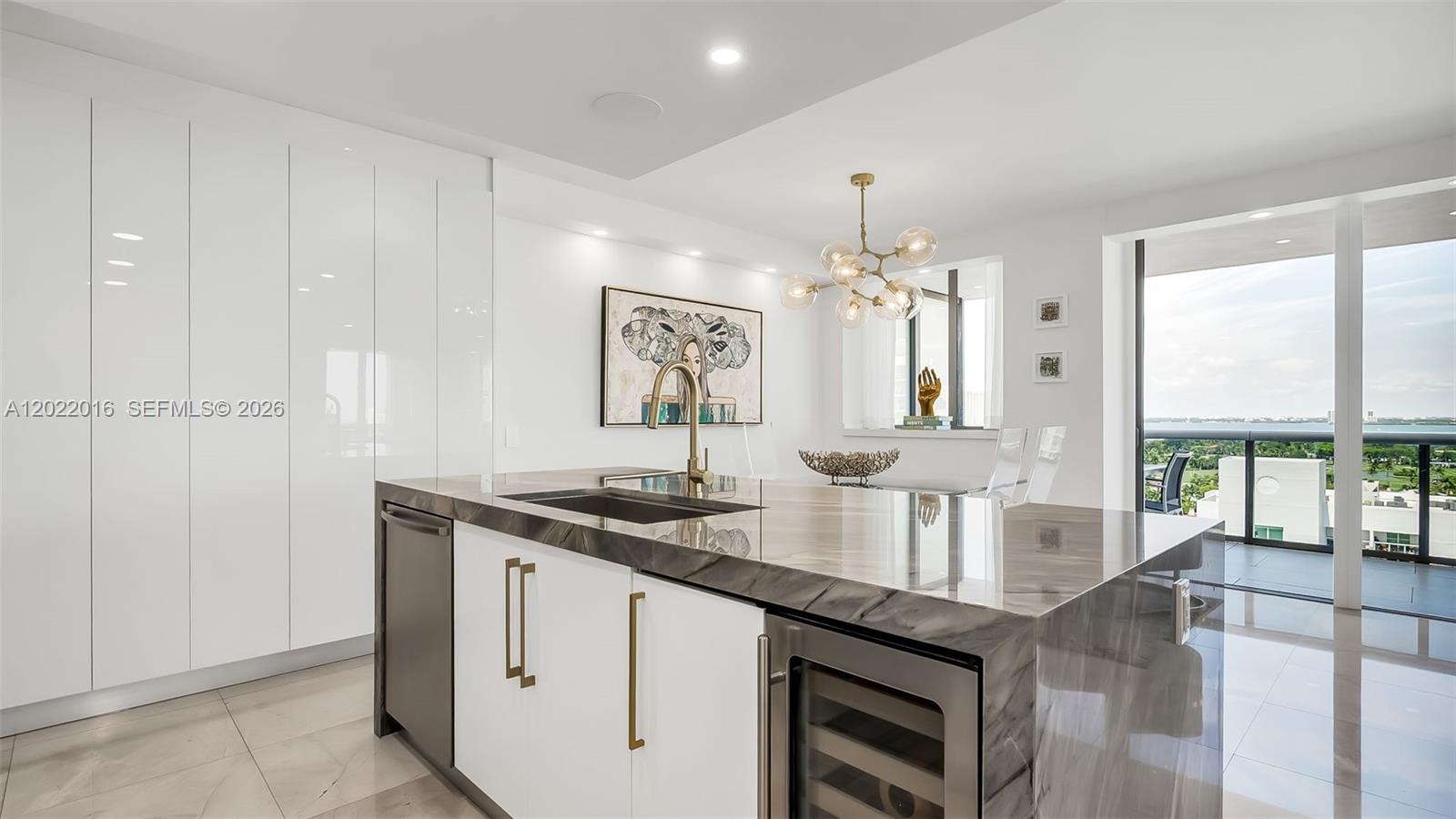 A modern living room features floor-to-ceiling windows, a balcony, white tile floors, and two chandeliers — 5875 Collins Ave # 1807, Miami Beach FL 33140, MIAMI BEACH, FL