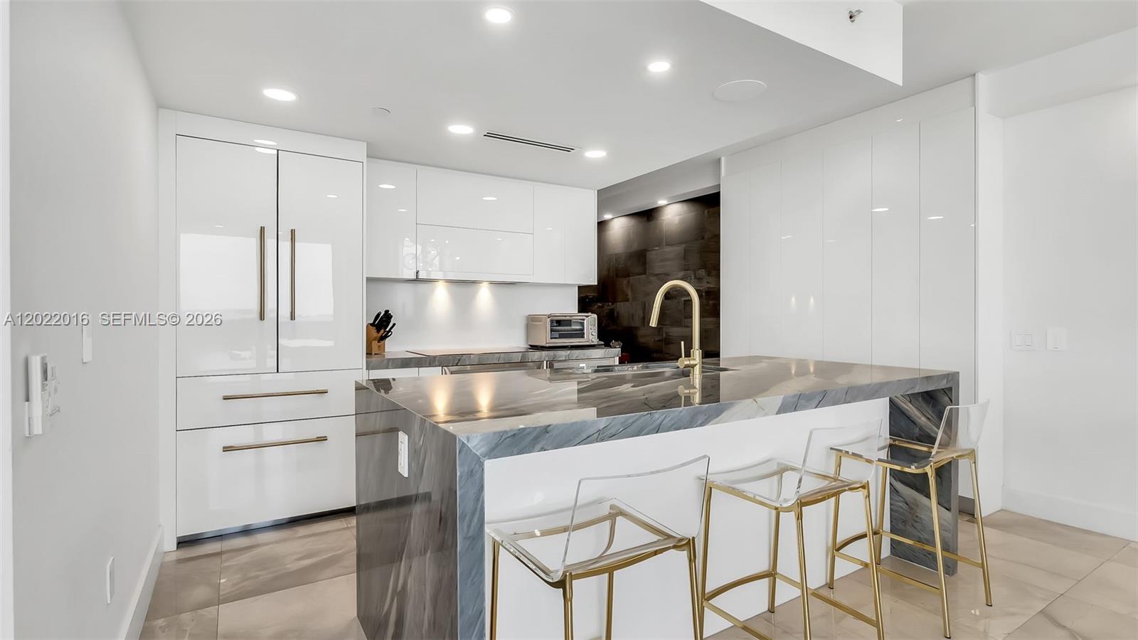 A modern kitchen features a marble-topped island, white cabinetry, and a balcony with water views — 5875 Collins Ave # 1807, Miami Beach FL 33140, MIAMI BEACH, FL