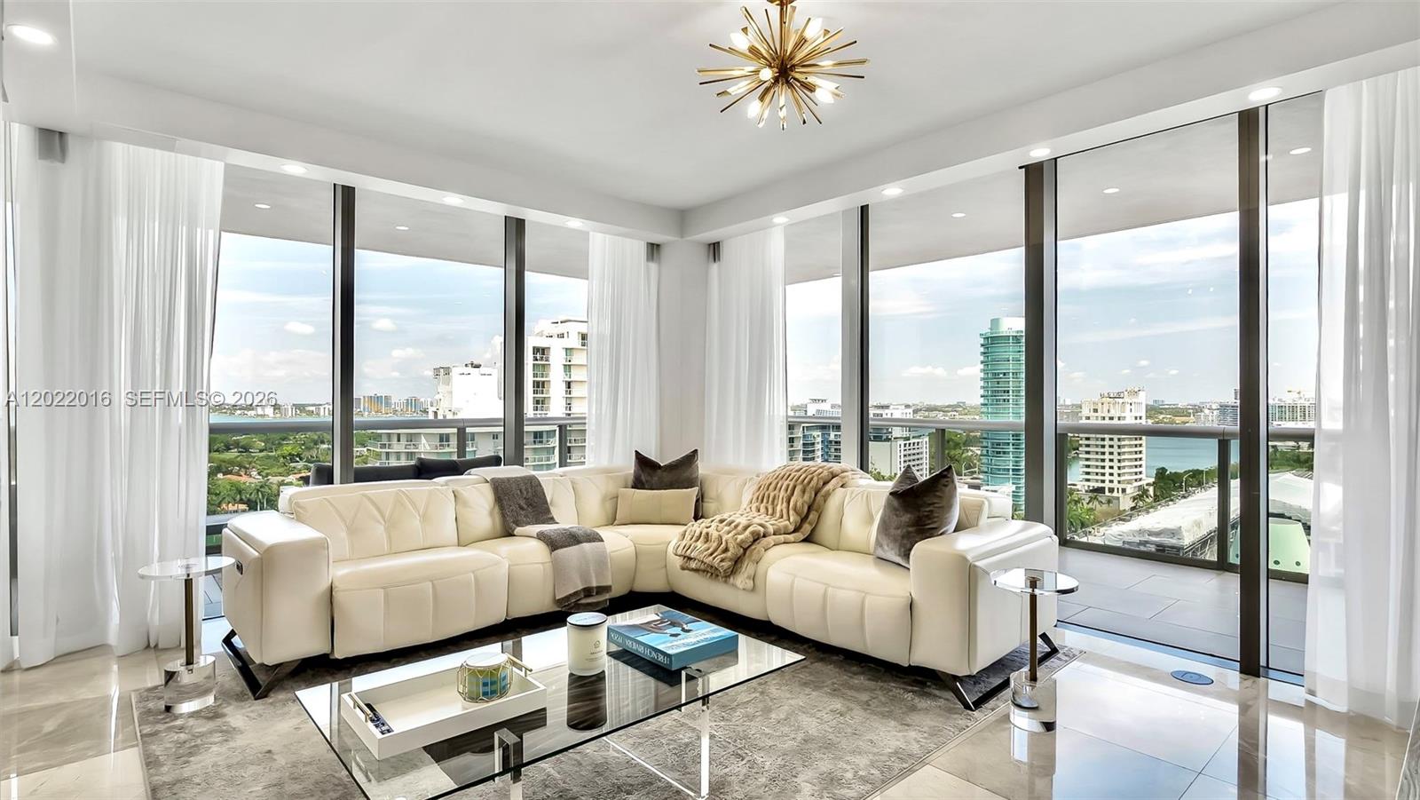 A modern kitchen features white cabinetry, a marble-topped island, and gold-toned bar stools — 5875 Collins Ave # 1807, Miami Beach FL 33140, MIAMI BEACH, FL