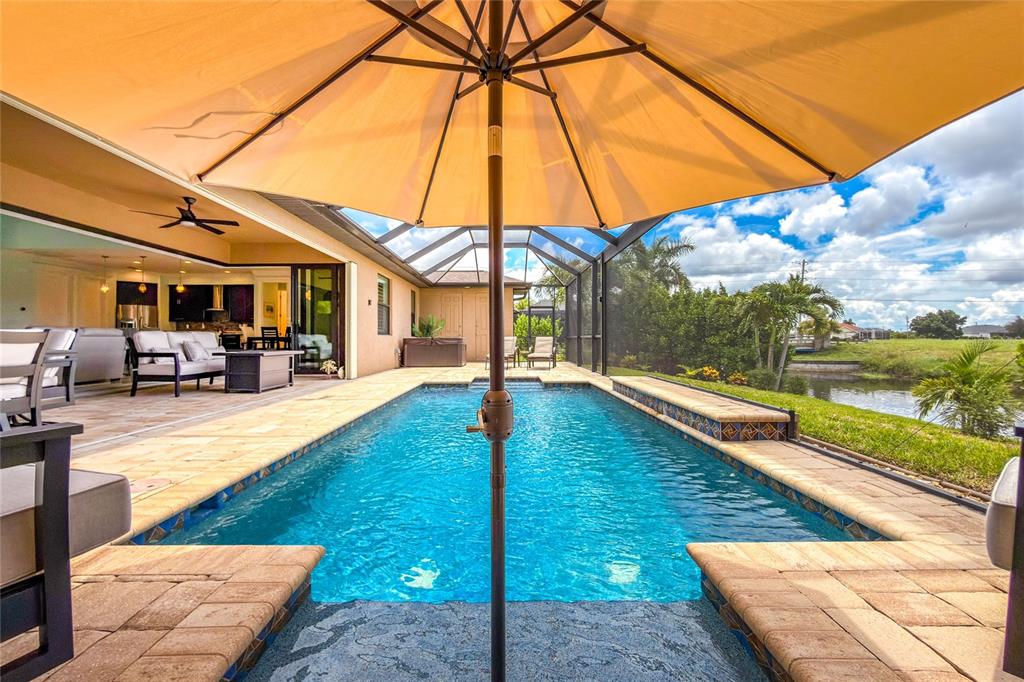 A swimming pool with a tan umbrella sits on a patio next to a house — 4 WHITE MARSH LANE, ROTONDA WEST, FL