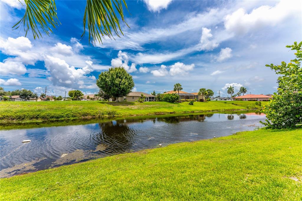 A grassy lawn slopes down to a canal with houses visible in the background — 4 WHITE MARSH LANE, ROTONDA WEST, FL