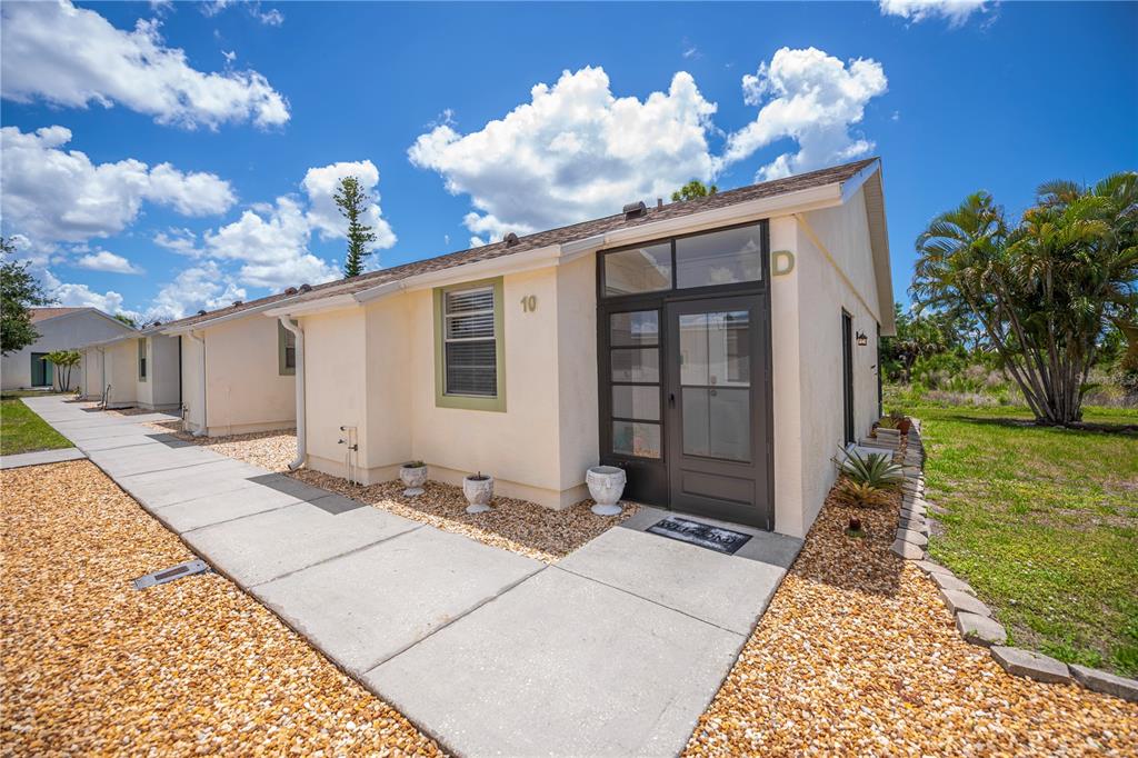 A single-story unit with a dark-framed glass door, a window, and a concrete walkway — 6796 GASPARILLA PINES BOULEVARD UNIT 10, ENGLEWOOD, FL