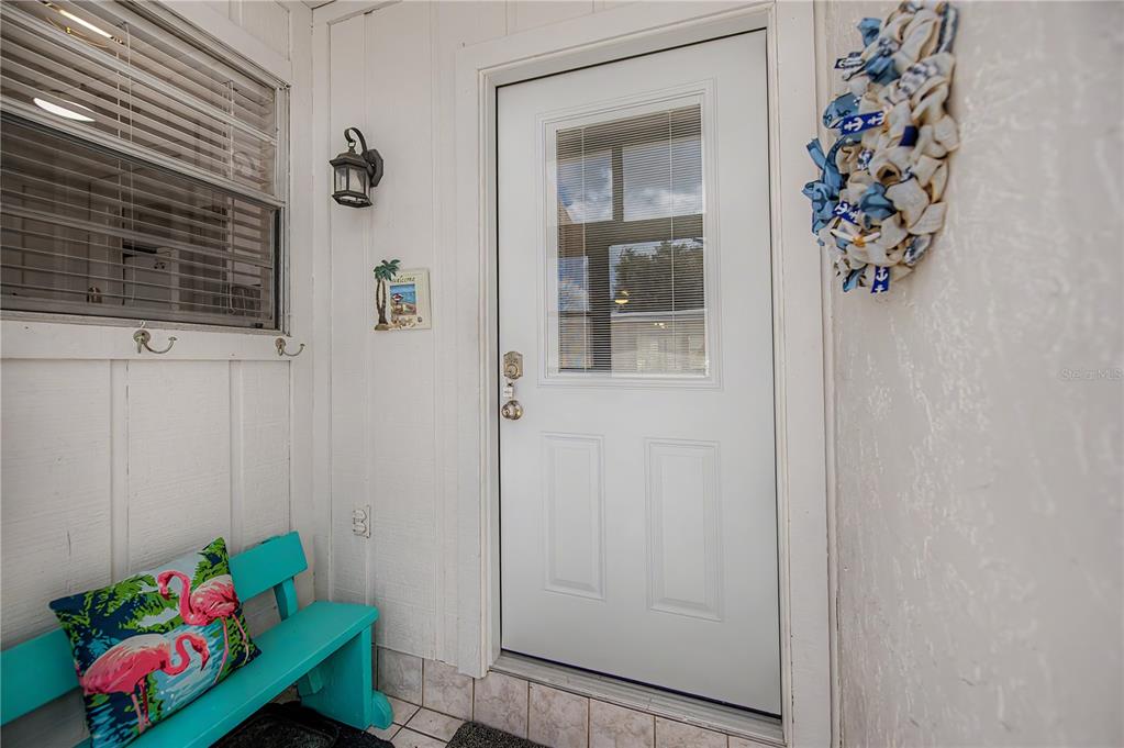 A white front door with a window sits on a porch next to a teal bench — 6796 GASPARILLA PINES BOULEVARD UNIT 10, ENGLEWOOD, FL
