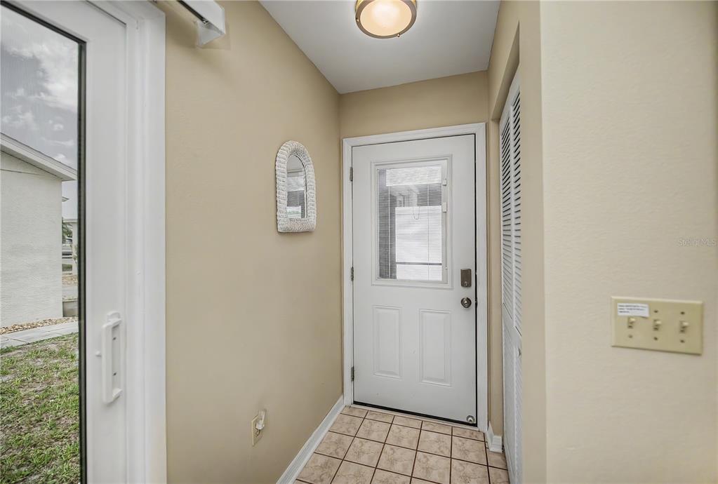 A tiled entryway features a white door, a wall-mounted mirror, and a light fixture — 6796 GASPARILLA PINES BOULEVARD UNIT 10, ENGLEWOOD, FL