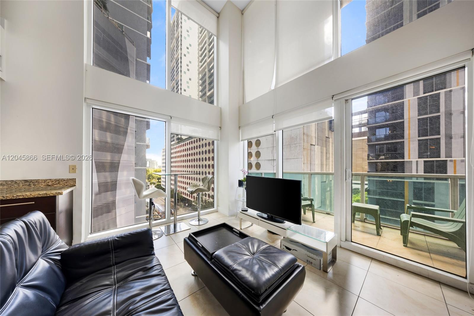 A living room features double-height windows, a black leather sofa, and a balcony — 41 SE 5th St # 502, Miami FL 33131, MIAMI, FL