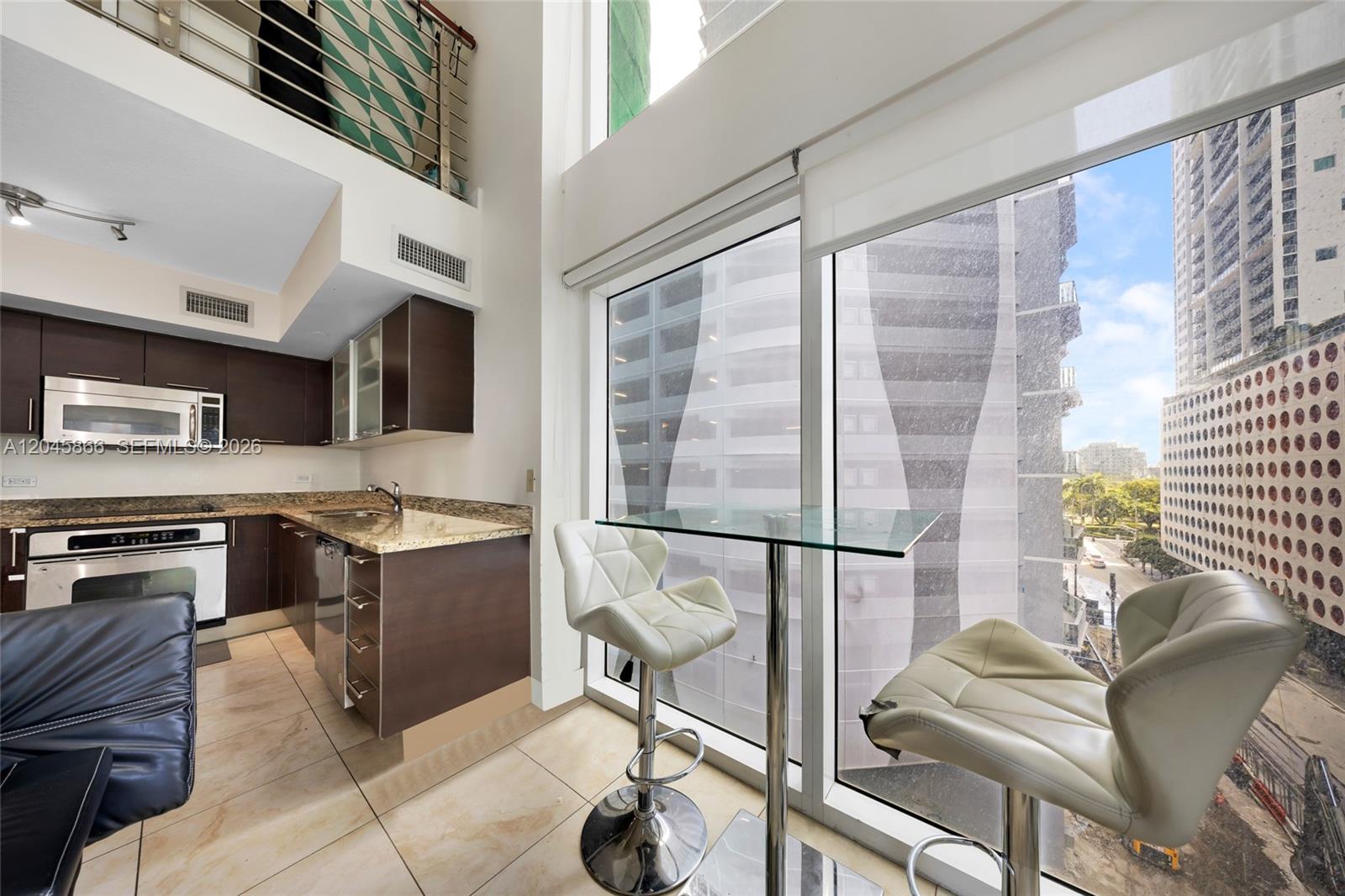 A modern kitchen with dark cabinetry and a glass breakfast table overlooking city buildings — 41 SE 5th St # 502, Miami FL 33131, MIAMI, FL
