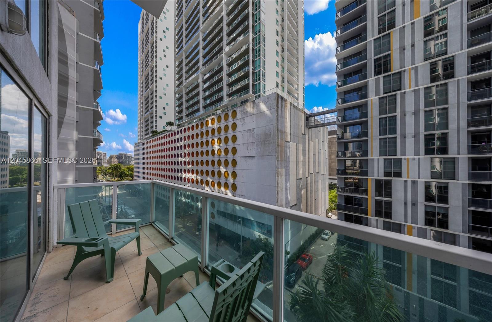 A balcony with green chairs and a small table overlooks a city street and buildings — 41 SE 5th St # 502, Miami FL 33131, MIAMI, FL