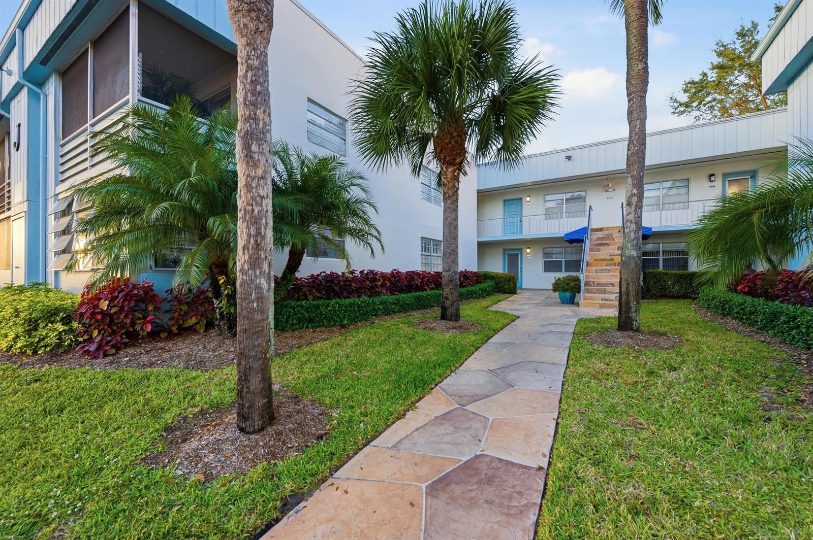 A stone walkway leads to the entrance of a two-story apartment building with palm trees — 442 Normandy J, Delray Beach FL 33484, DELRAY BEACH, FL