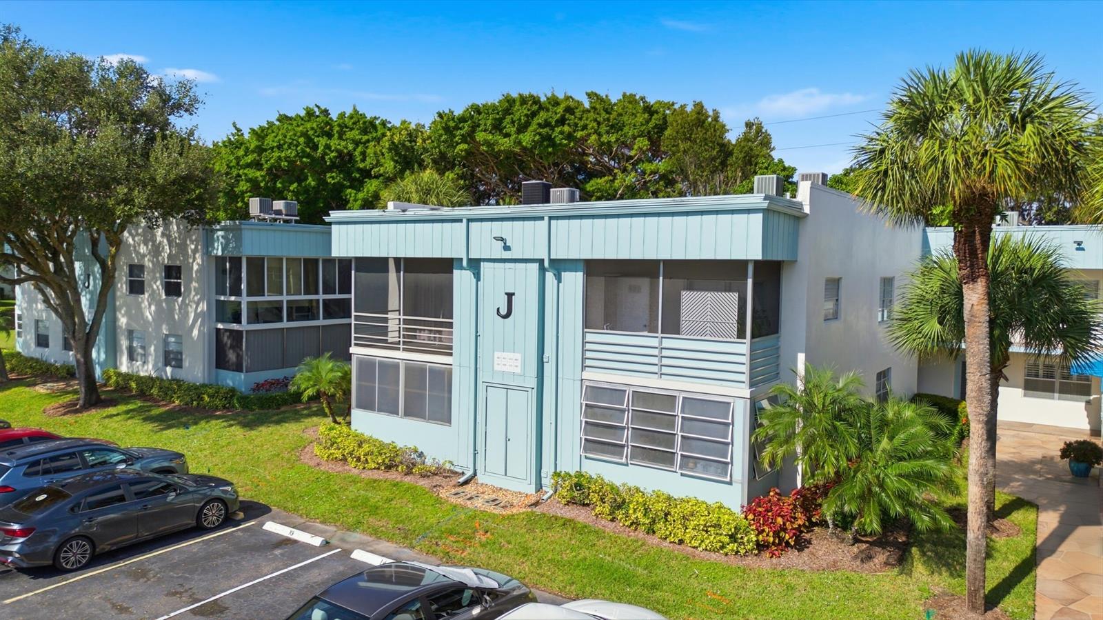 An exterior view of a two-story light blue apartment building with screened balconies and parking — 442 Normandy J, Delray Beach FL 33484, DELRAY BEACH, FL