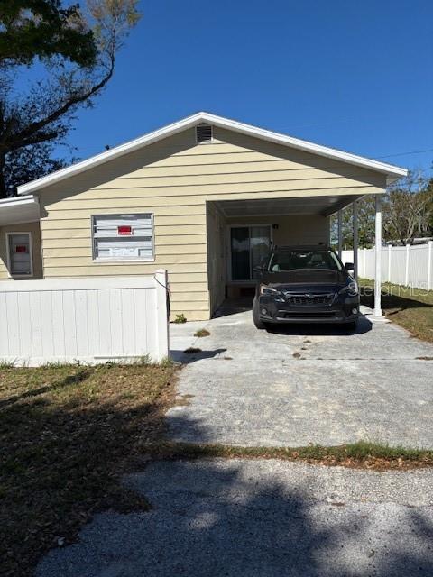 A tan house with a carport and a white fence sits on a concrete driveway — 9145 RALLY LANE, HOLIDAY, FL
