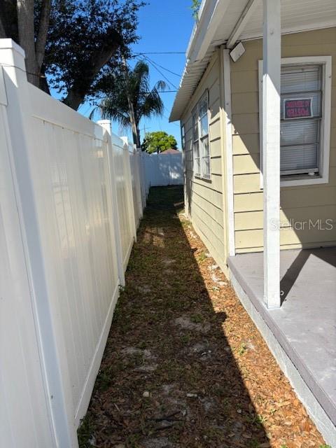 A narrow dirt path runs between a white vinyl fence and the side of a house — 9145 RALLY LANE, HOLIDAY, FL