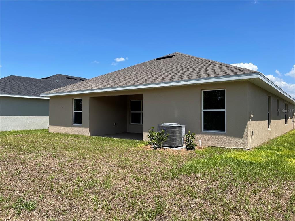The rear exterior of a tan stucco house features a covered patio and an AC unit — 7630 BENT TREE LOOP, ST CLOUD, FL