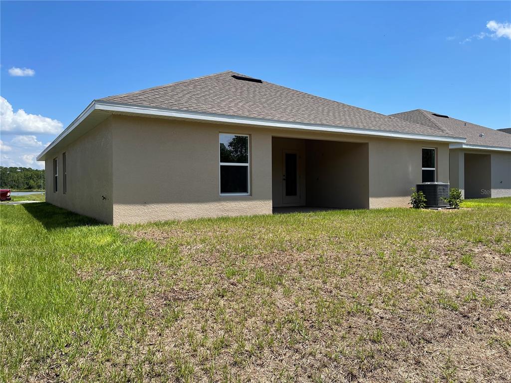 The rear exterior of a beige stucco house features a covered patio and a grassy yard — 7630 BENT TREE LOOP, ST CLOUD, FL