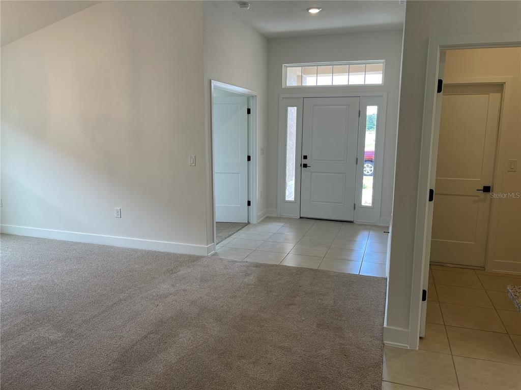 An entryway with tile flooring, a white front door, and adjacent carpeted living space — 7630 BENT TREE LOOP, ST CLOUD, FL