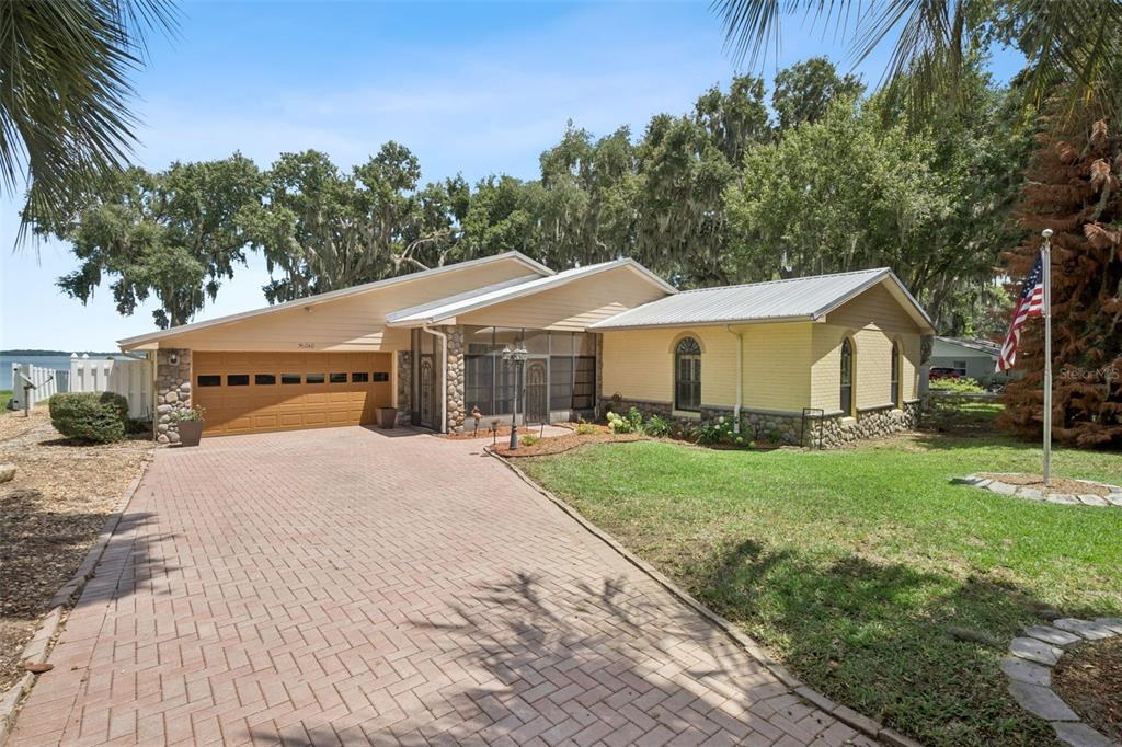 A single-story house with a brick driveway, yellow siding, and a metal roof — 35040 SHADY OAKS LANE, FRUITLAND PARK, FL