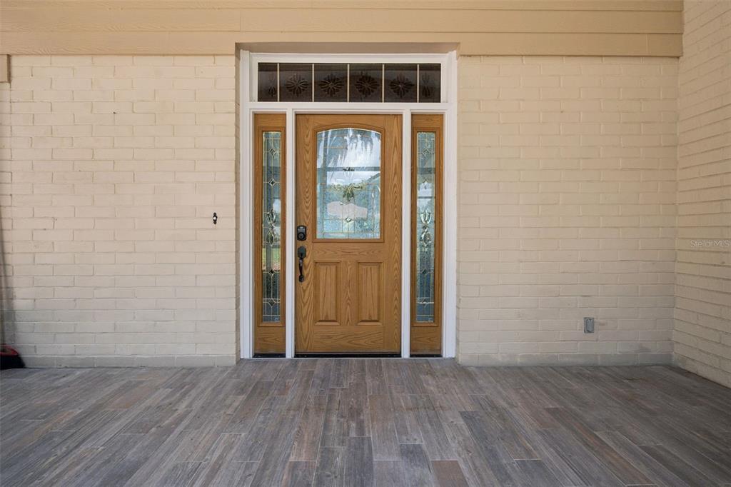 A wooden front door with glass panels and sidelights is set into a beige brick wall — 35040 SHADY OAKS LANE, FRUITLAND PARK, FL