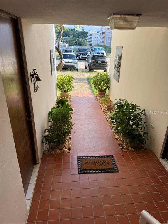 An outdoor walkway leads from a tiled entryway toward a parking area with potted plants — Codominium VISTA REAL UNIT 9, FAJARDO, PR