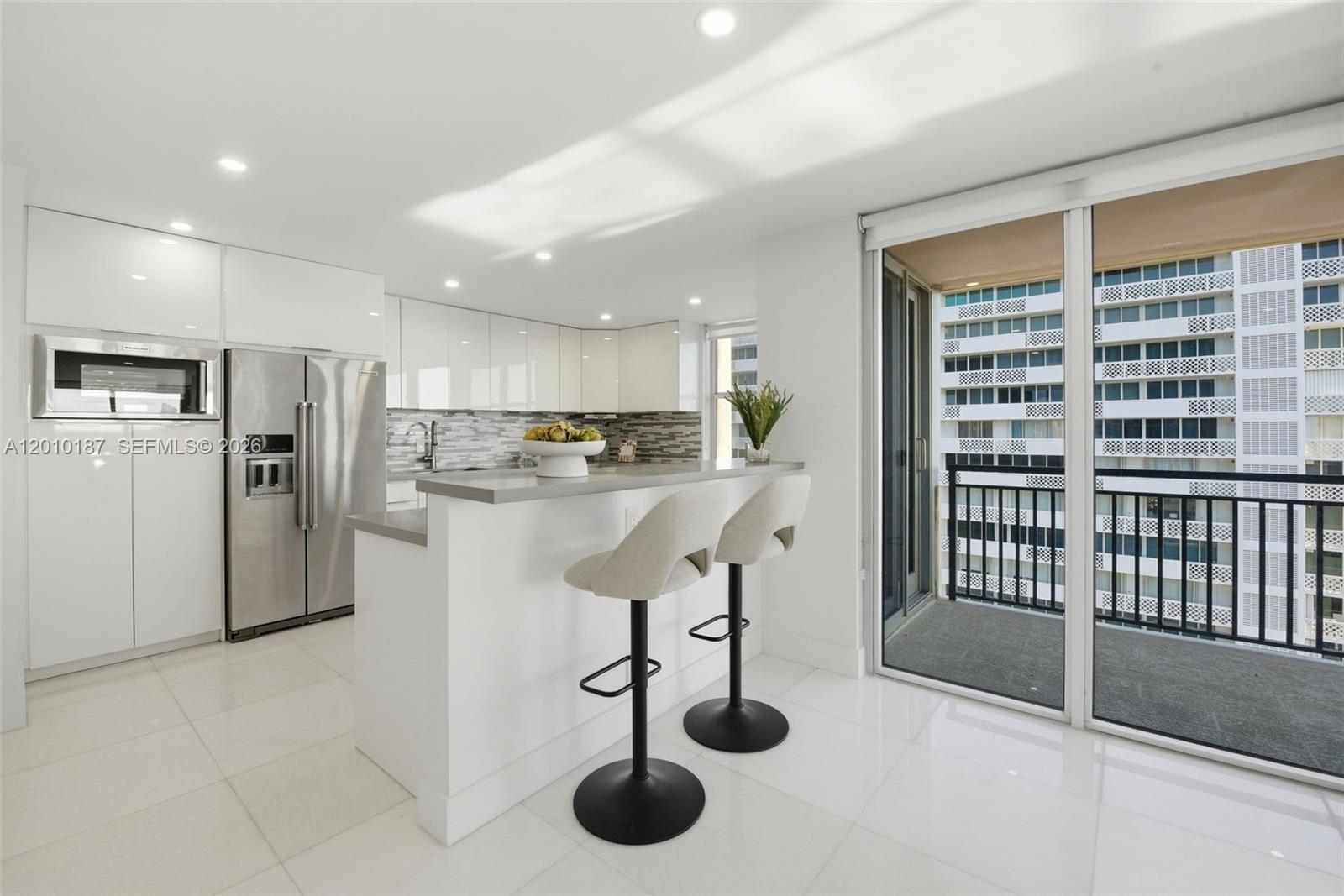 A modern kitchen features white cabinetry, stainless steel appliances, a breakfast bar, and a balcony — 1180 S Ocean Boulevard # 12F, Boca Raton FL 33432, BOCA RATON, FL