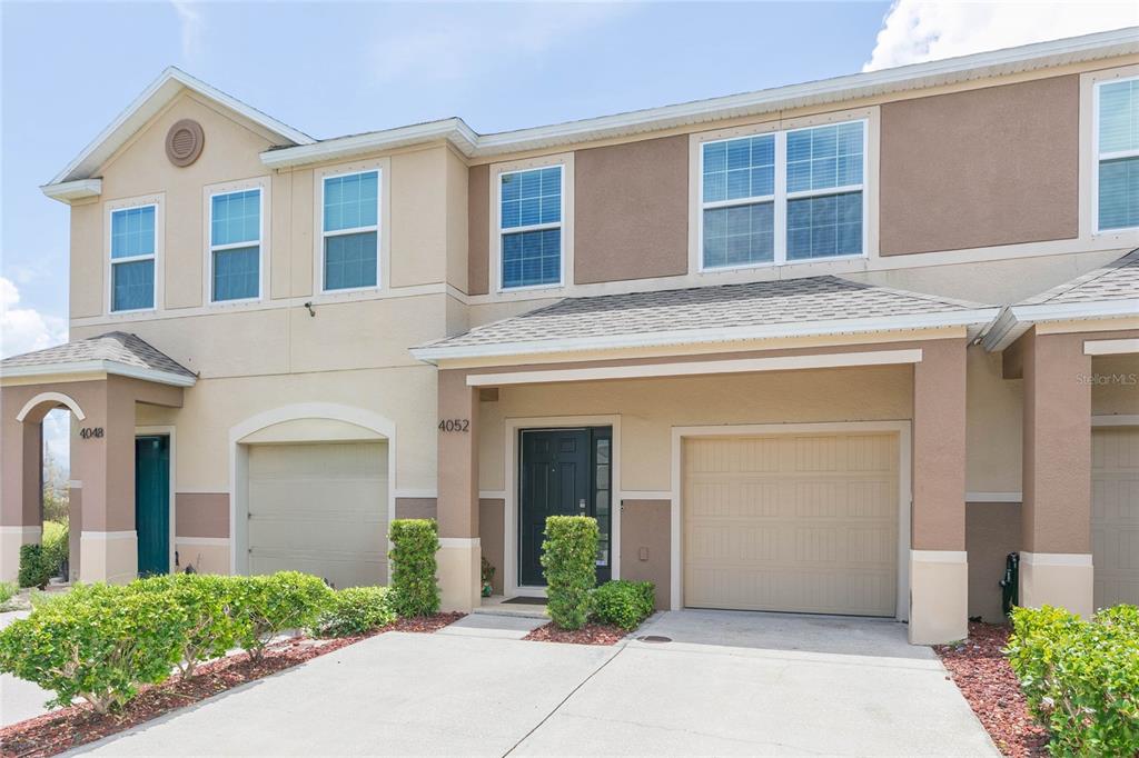 A two-story townhouse exterior features tan stucco walls, a garage, and a front entrance — 4052 70TH TERRACE N, PINELLAS PARK, FL