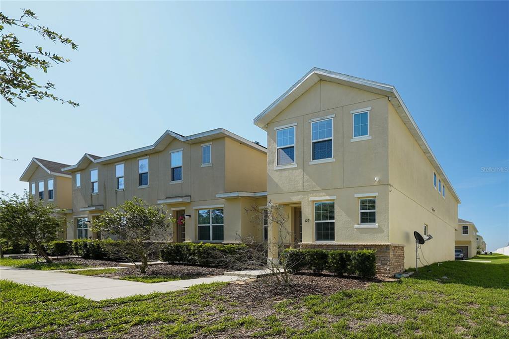 A row of two-story yellow stucco townhouses with stone accents and a concrete walkway — 129 HOLLY VILLAGE DRIVE, DAVENPORT, FL