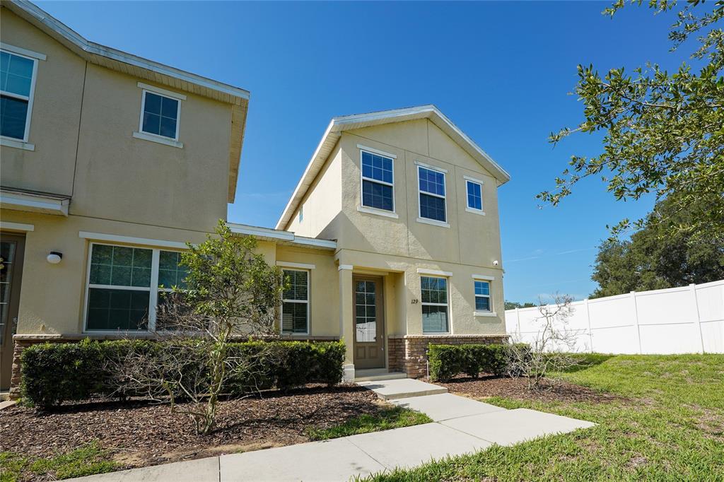A two-story tan stucco townhouse with a front entrance and a small landscaped yard — 129 HOLLY VILLAGE DRIVE, DAVENPORT, FL