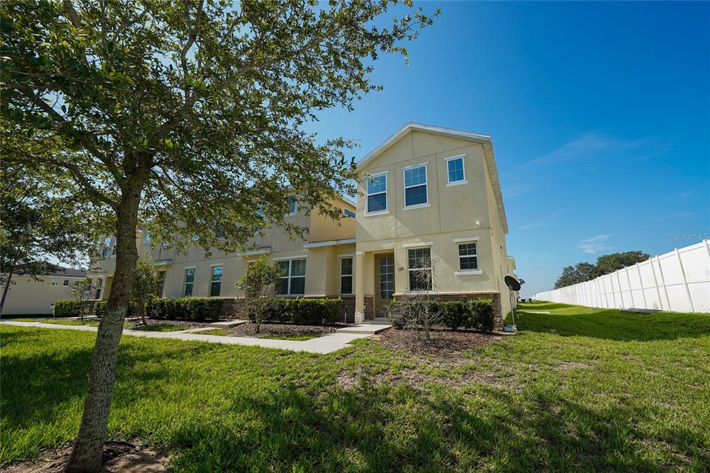 A two-story tan townhouse with a stone facade and a white vinyl fence nearby — 129 HOLLY VILLAGE DRIVE, DAVENPORT, FL