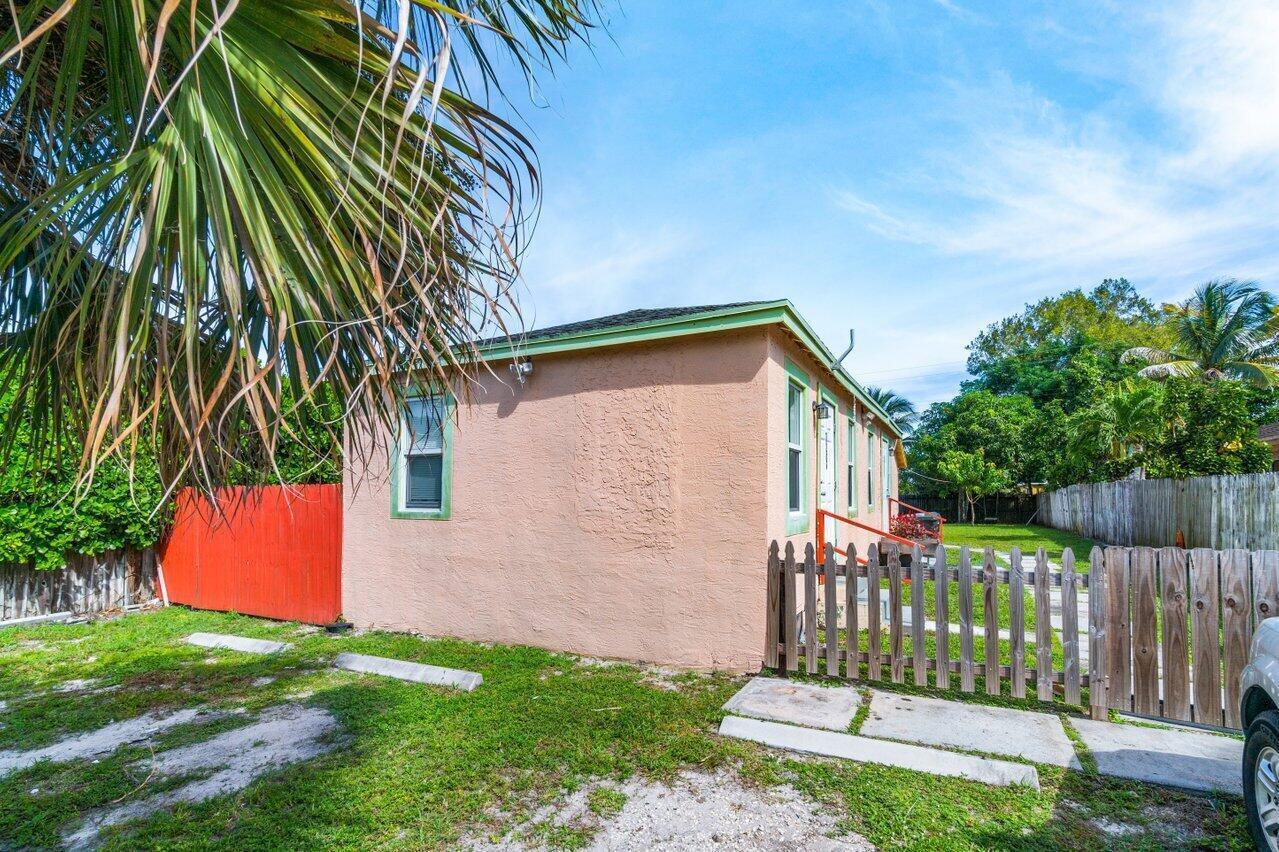 A peach-colored house exterior features a small wooden fence and a red privacy fence — 320 Swain Boulevard, FL 33463, FL